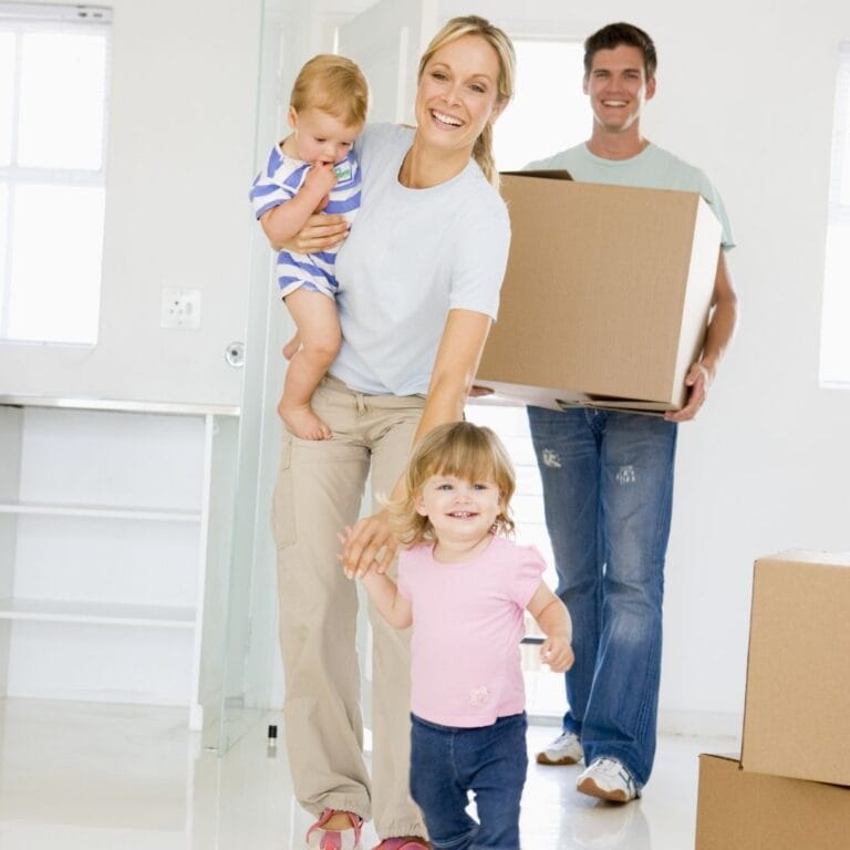 smiling family walking into new home carrying boxes