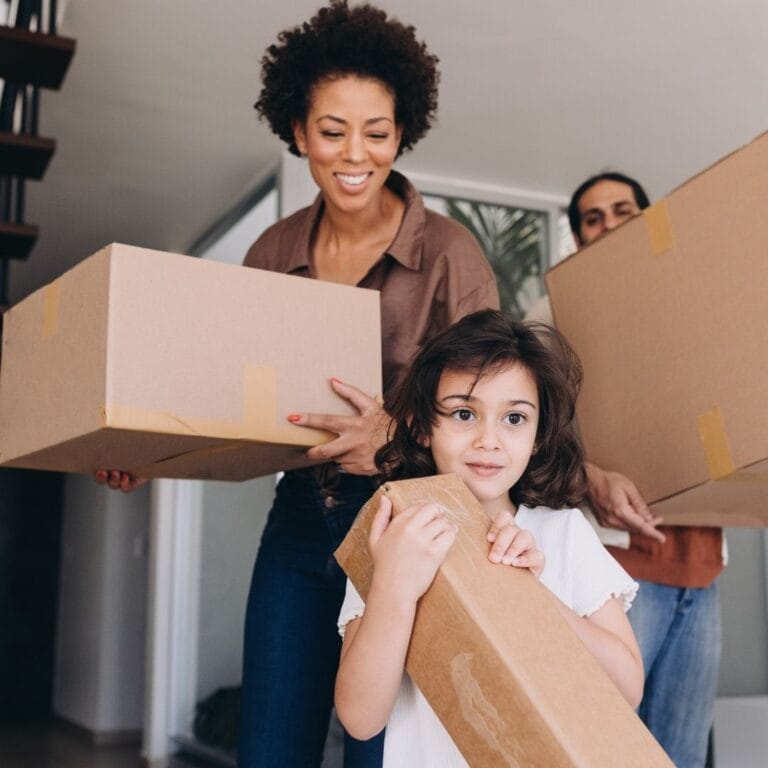 family waking into house with moving boxes